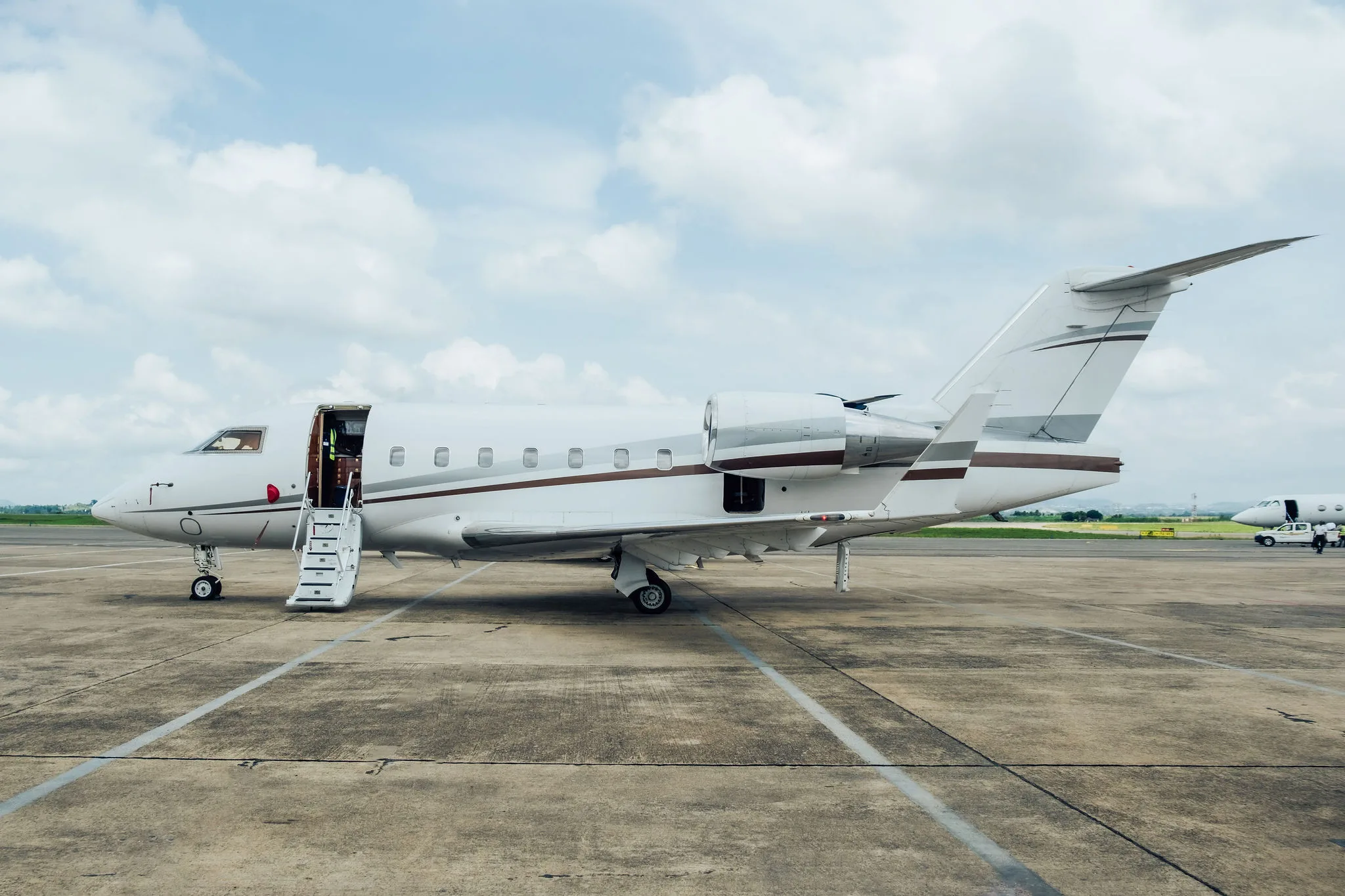 A white Bombardier Challenger business jet with brown stripes on the tarmac, door open with stairs extended.