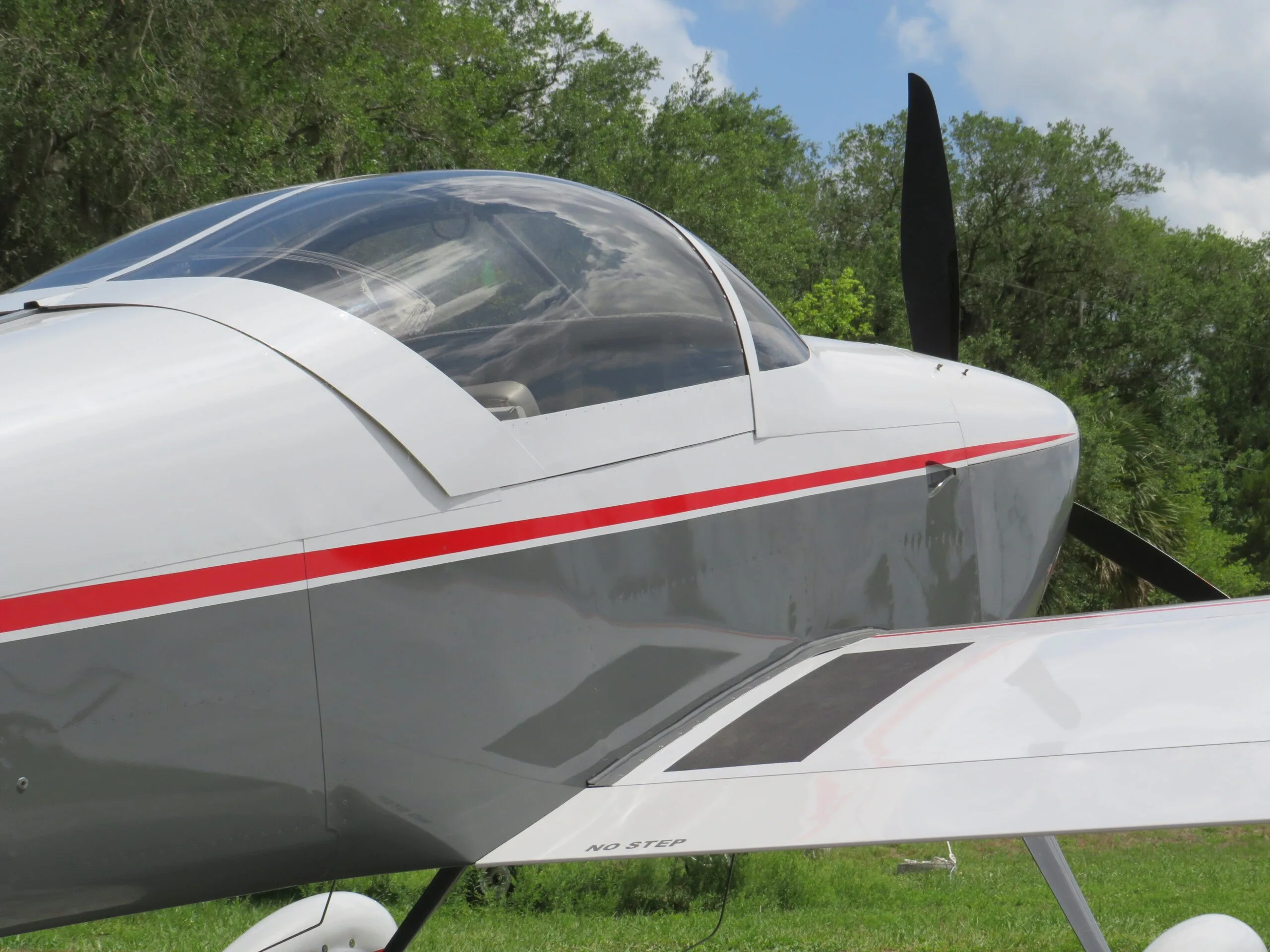Close-up side view of the cockpit canopy and wing of a white and grey aircraft with a red stripe.