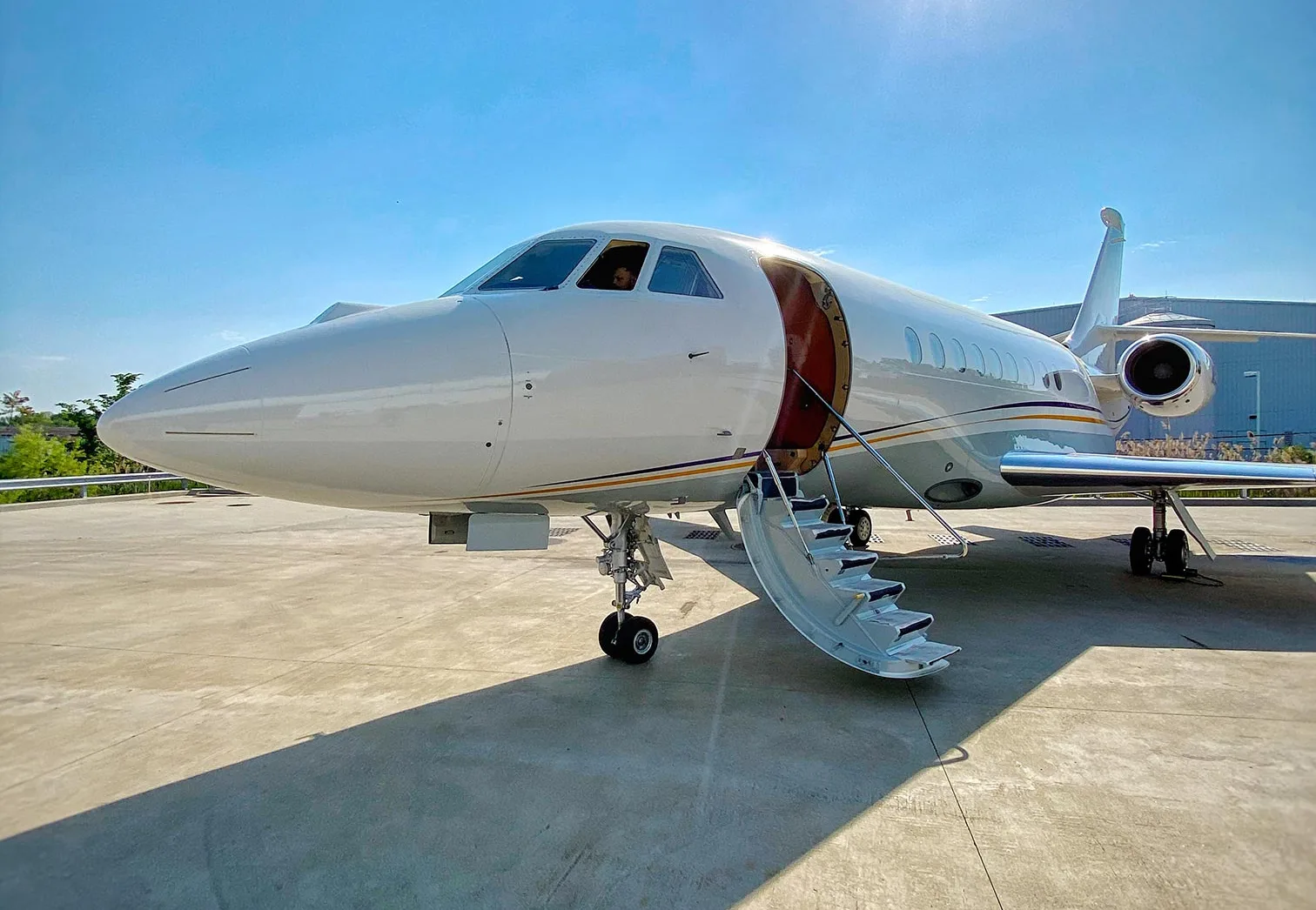 A white business jet with two rear-mounted engines flies over a misty, forested landscape.