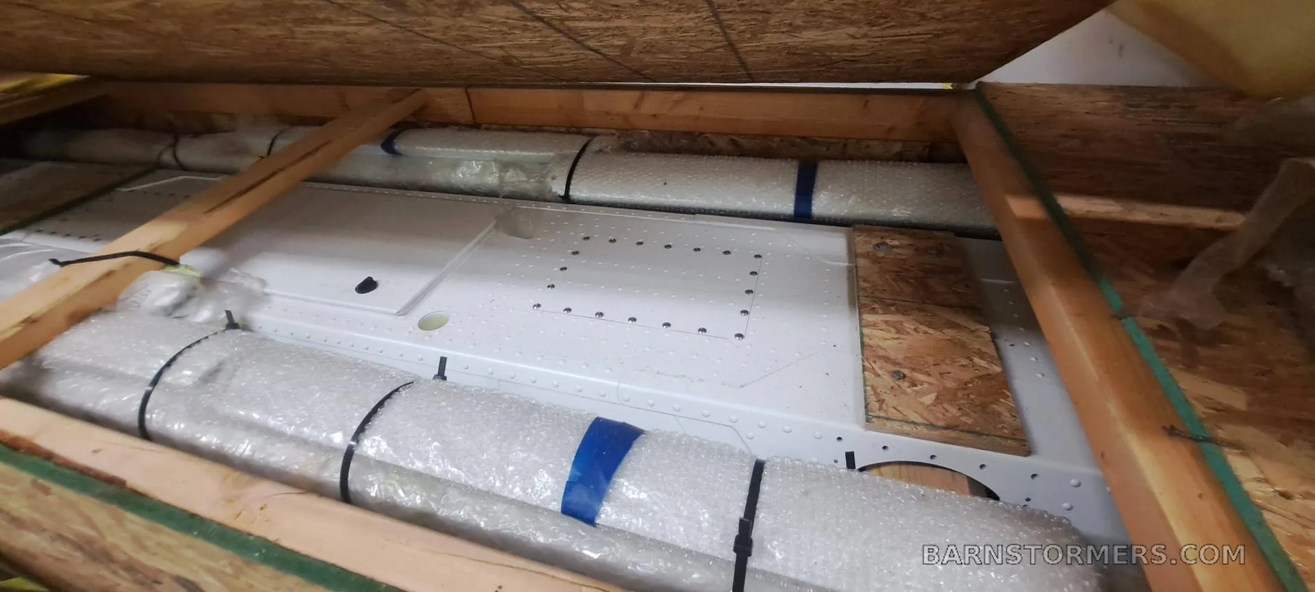 Aircraft components, wrapped in bubble wrap and secured with blue tape, packed inside a wooden shipping crate.