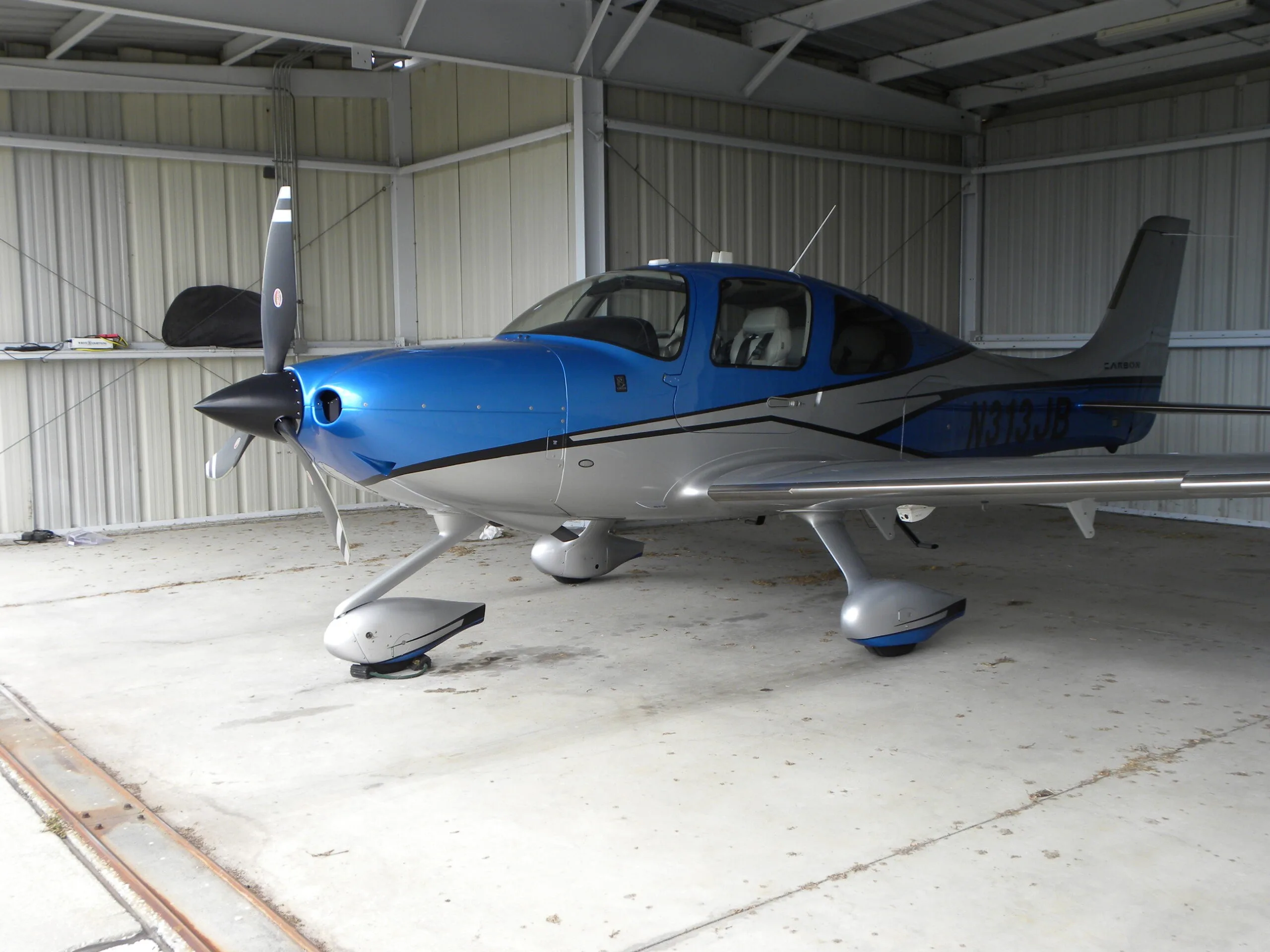 A blue and silver Cirrus SR22T aircraft, N313JB, parked inside a hangar.