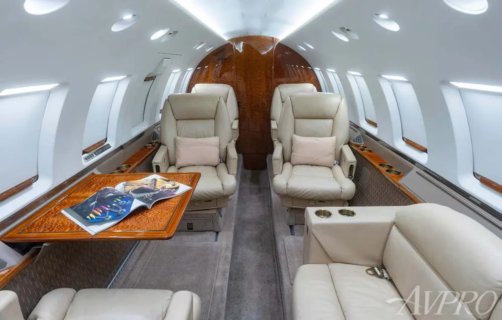 The luxurious interior cabin of a private jet features beige leather seats and a polished wooden table.