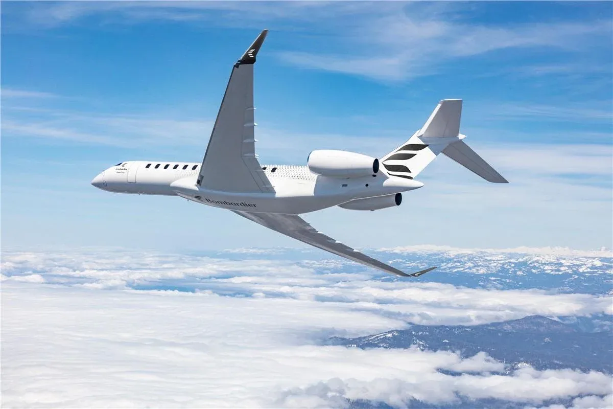A white Bombardier Global business jet with black tail markings flies over snow-capped mountains and clouds.