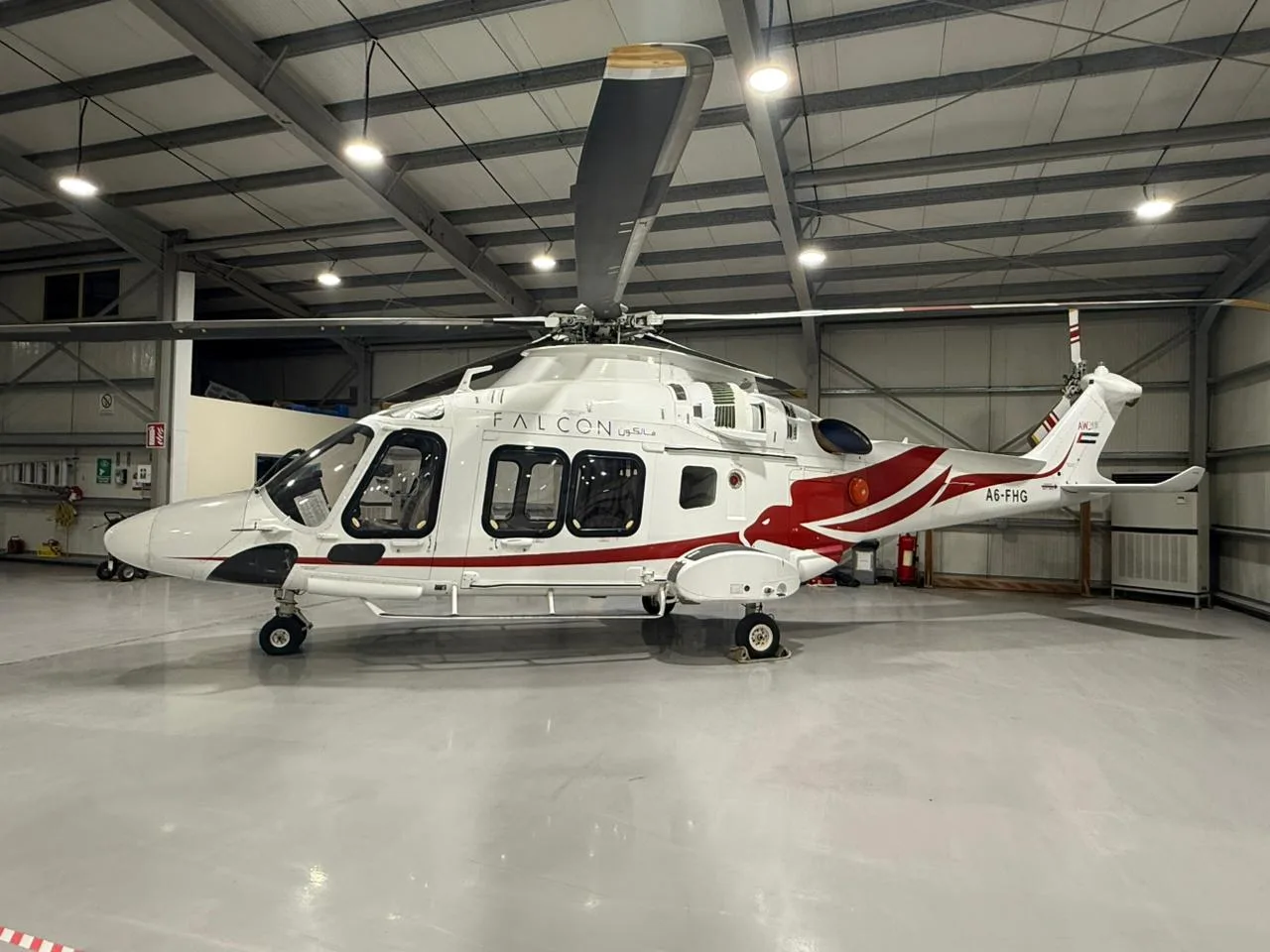 A6-FHG helicopter parked inside a hangar with white and red paint scheme.