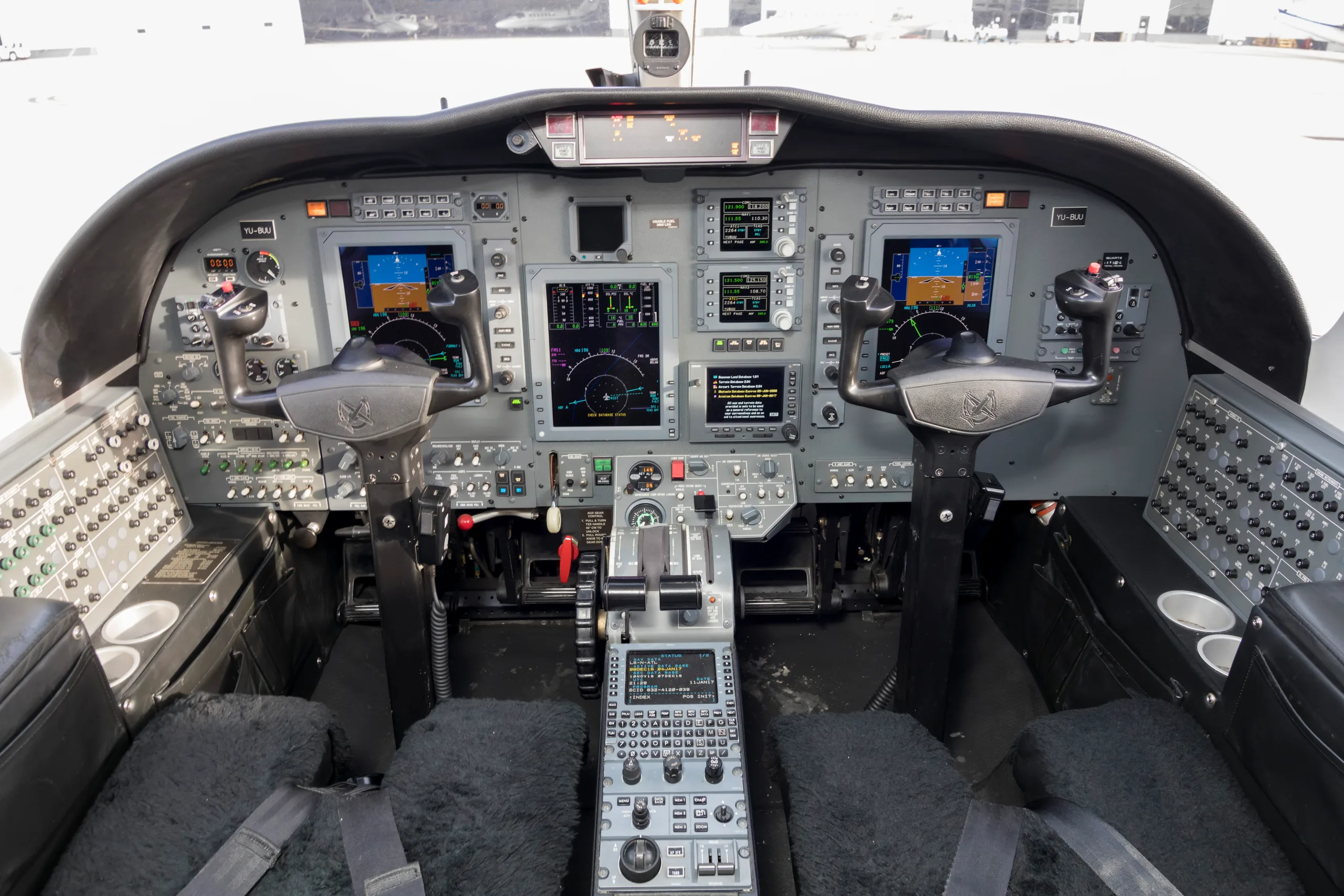 The cockpit of a private jet, featuring multiple digital displays, control yokes, and a central throttle quadrant.