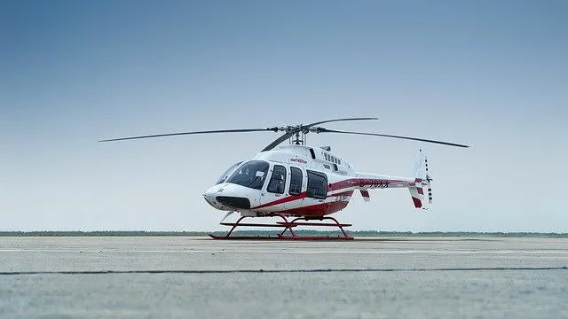 A white and red helicopter with skids on a tarmac under a clear blue sky, viewed from the front-right.