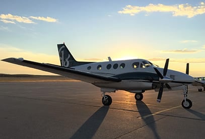 Side view of a Beechcraft King Air on the tarmac at sunset.