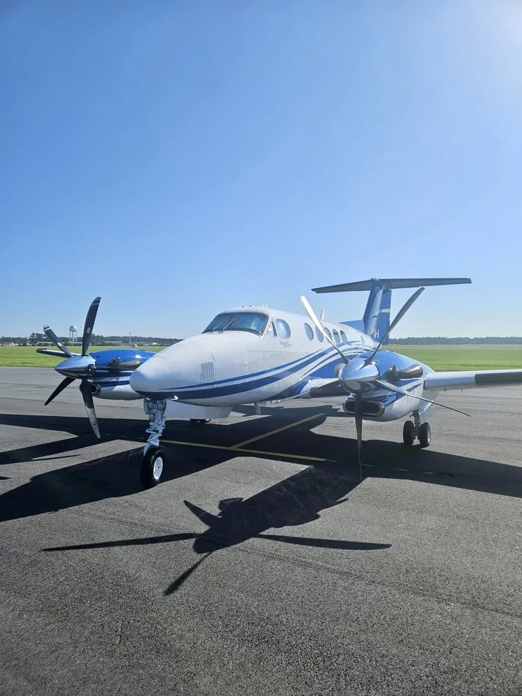 A white and blue Beechcraft King Air 350i aircraft with tail number N3AH parked on an airfield, viewed from the front.