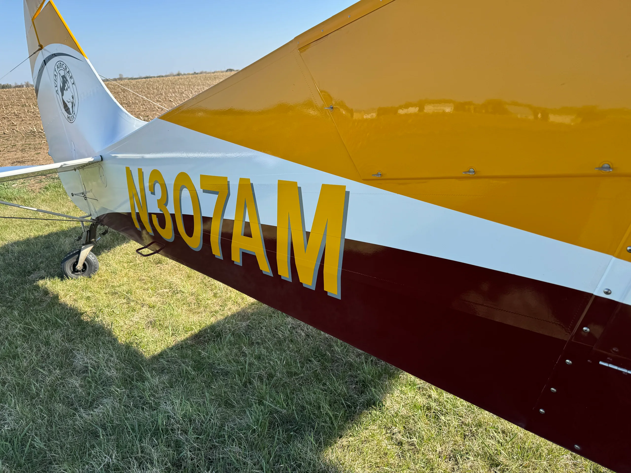 Close-up of the tail section of an Aviat Aircraft Husky A-1B, displaying its yellow, white, and maroon paint scheme and registration N307AM.