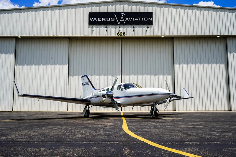 A Cessna 421 Golden Eagle aircraft is parked in front of a hangar with the Vaerus Aviation logo.