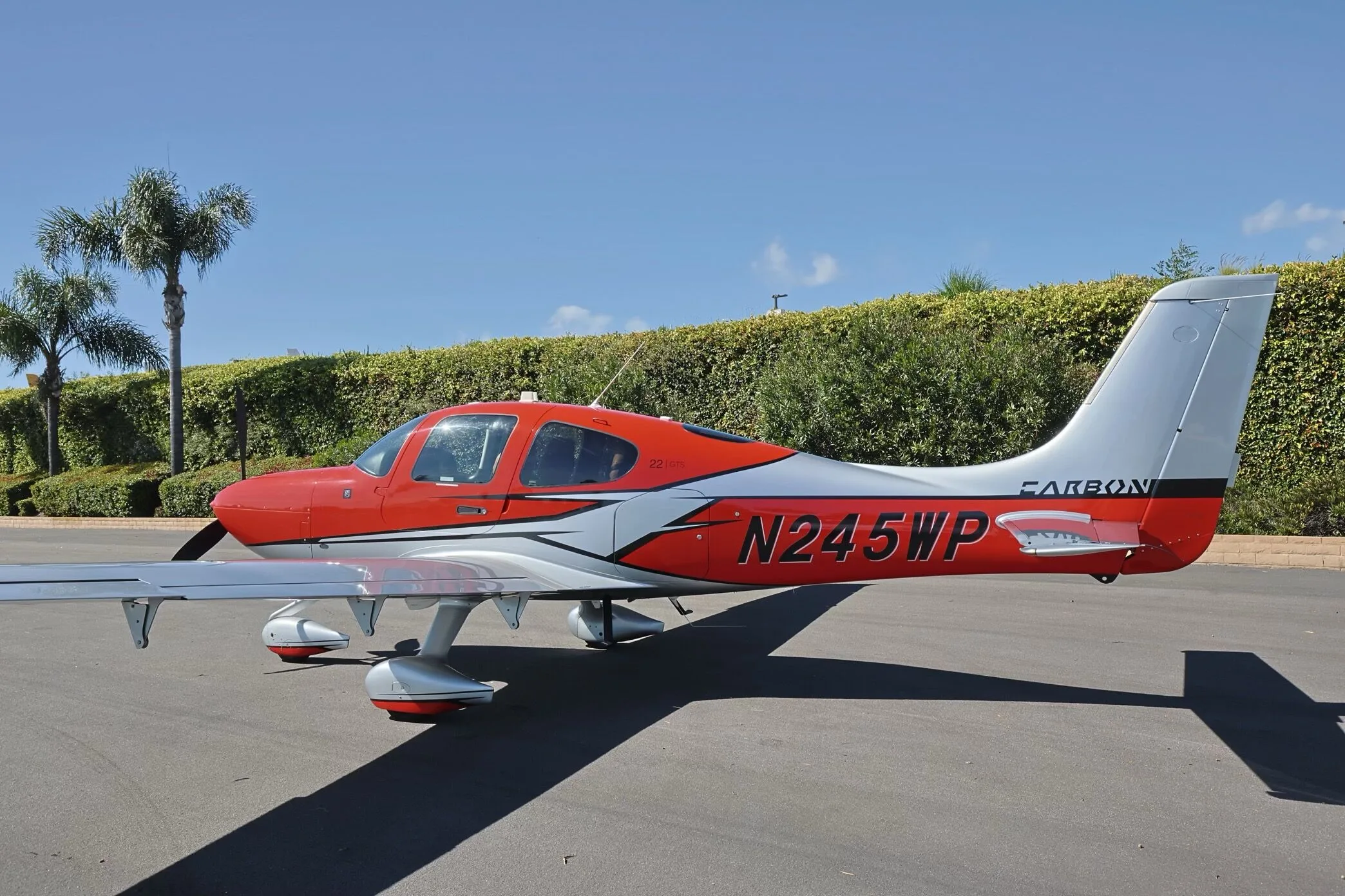 A red and silver Cirrus SR22 GTS aircraft, N245WP, parked on an tarmac with palm trees in the background.