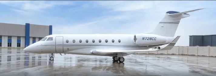 A white Gulfstream business jet, registration N728CC, parked on a wet tarmac with a hangar in the background.