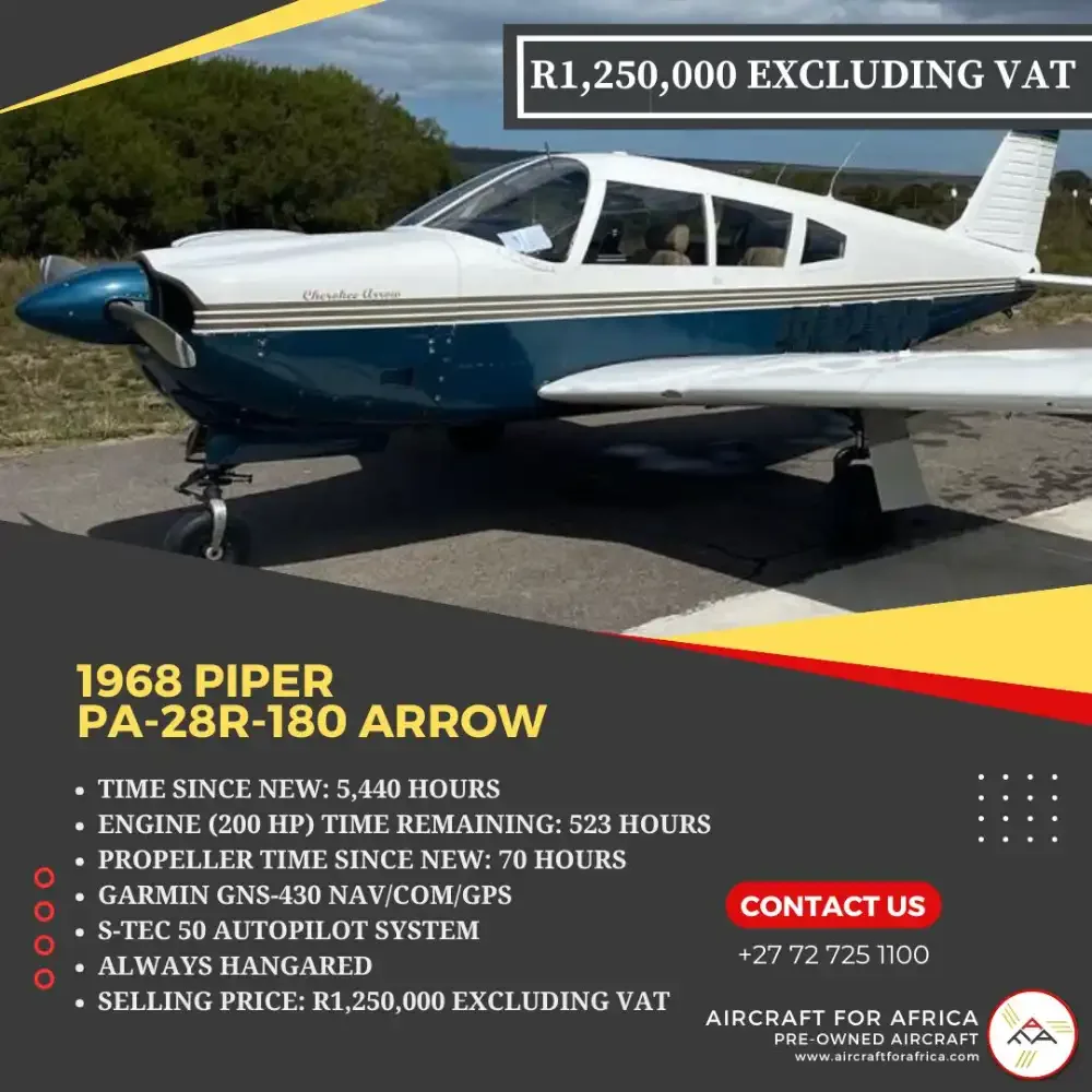 A white and blue Piper PA-28R-180 Arrow aircraft is parked on an airfield with trees in the background.