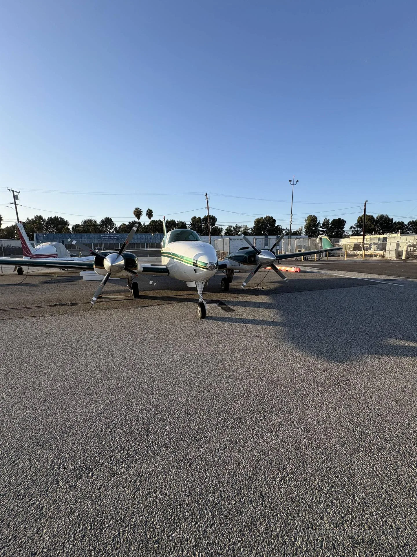 A white and green twin-engine propeller aircraft (N677Z) viewed from a low angle, parked on an asphalt ramp.