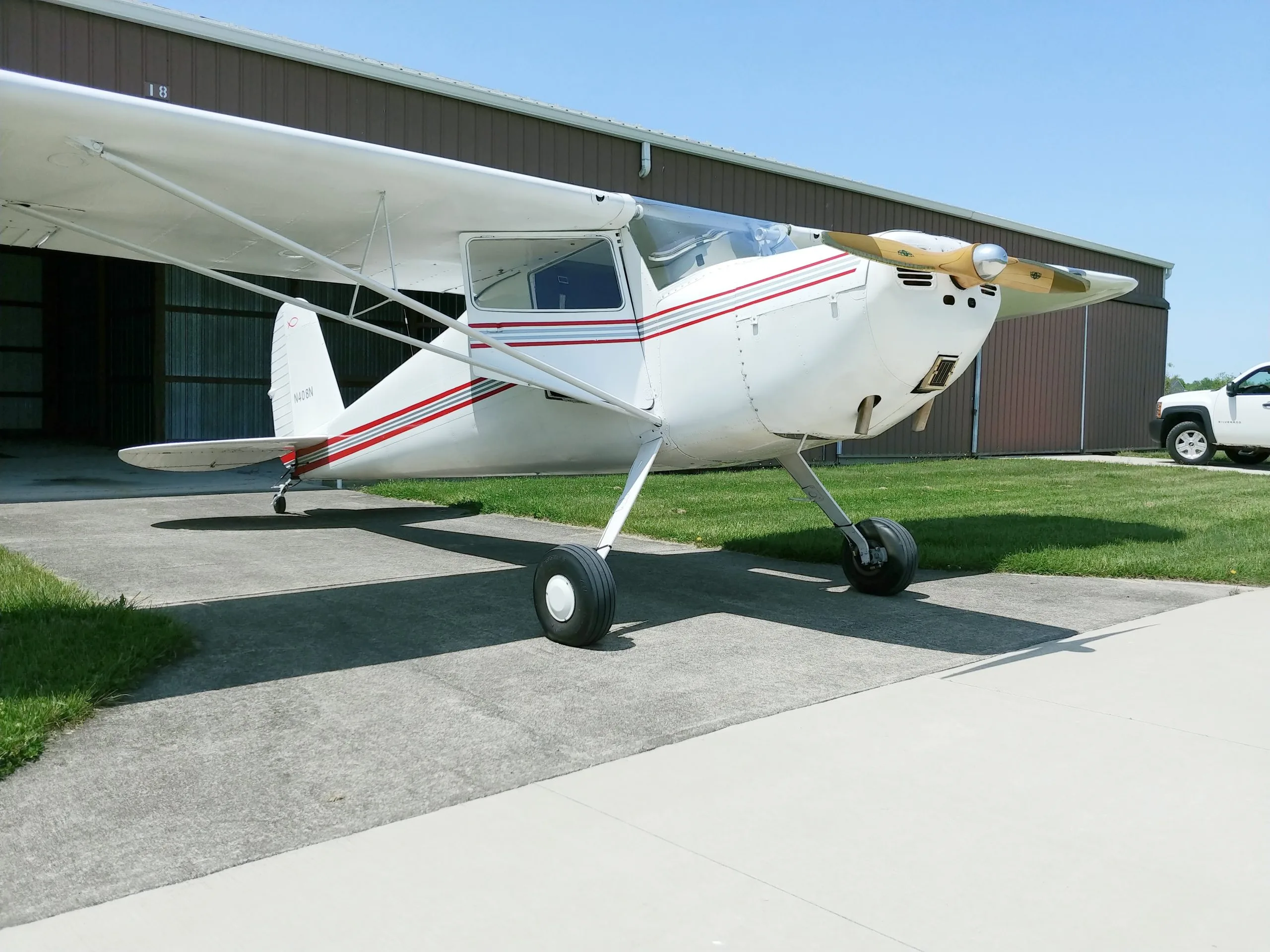 A white and red painted aircraft is parked on the tarmac in front of a hangar.