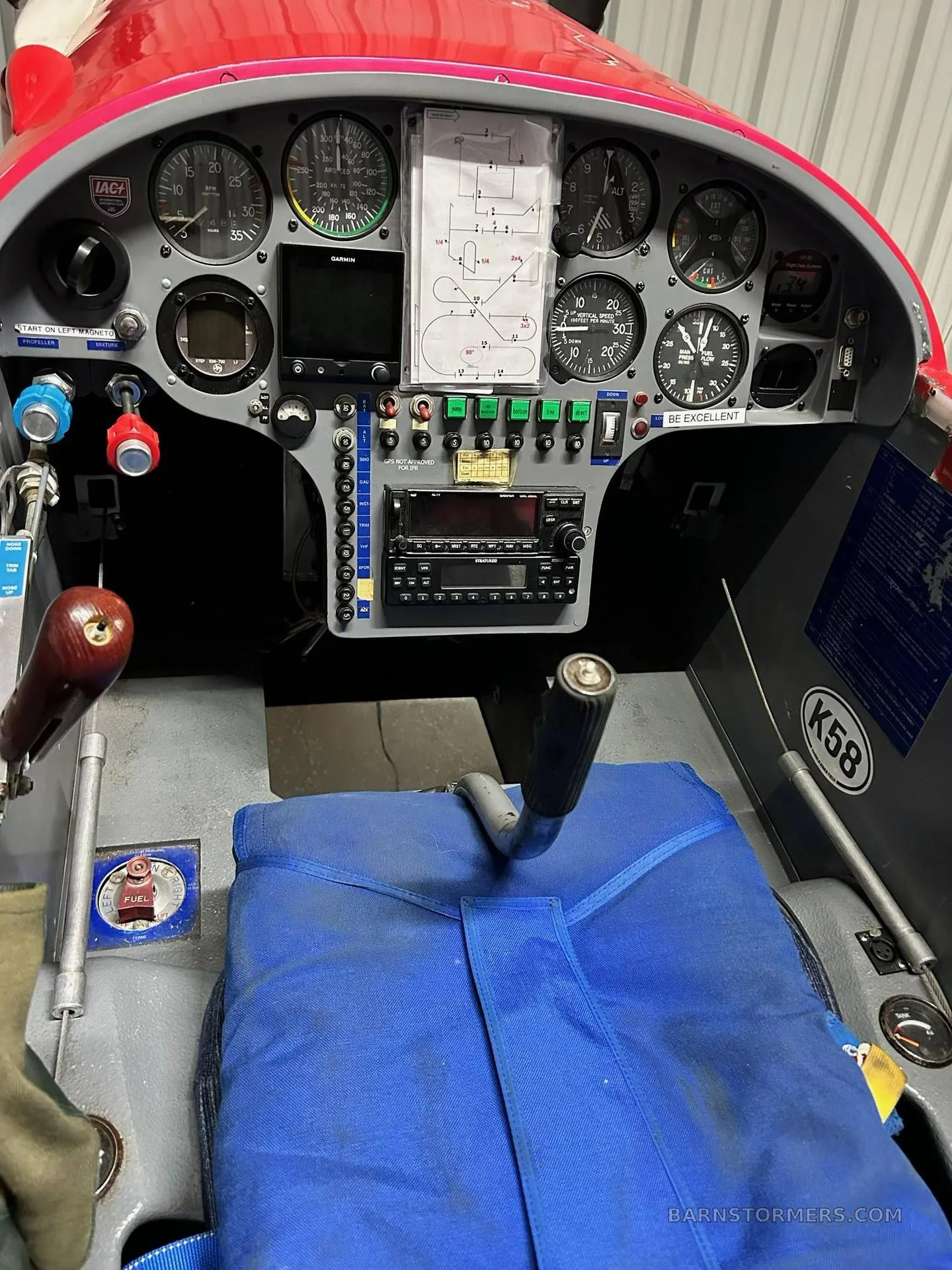 The cockpit of an aerobatic aircraft, showing the instrument panel with various gauges, a Garmin display, and a flight diagram.