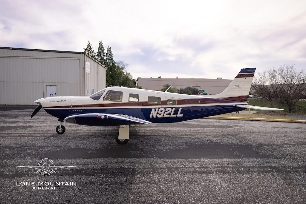 A side view of the Piper Saratoga II TC aircraft (N92LL) with blue and white paint scheme parked on an asphalt apron.