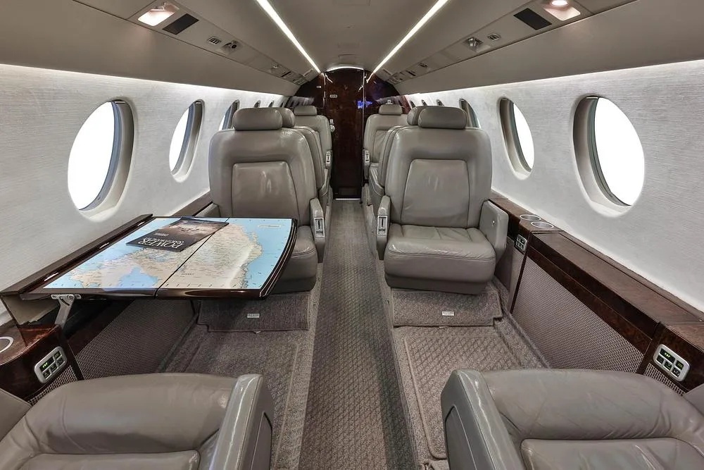 The luxurious cabin interior of a business jet with grey leather seats and a table displaying a map.