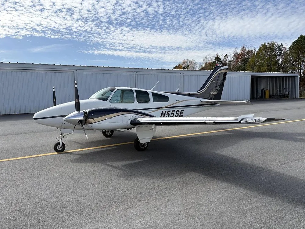 A white and dark blue twin-engine aircraft with registration N55SE is parked on the tarmac, viewed from the front left.