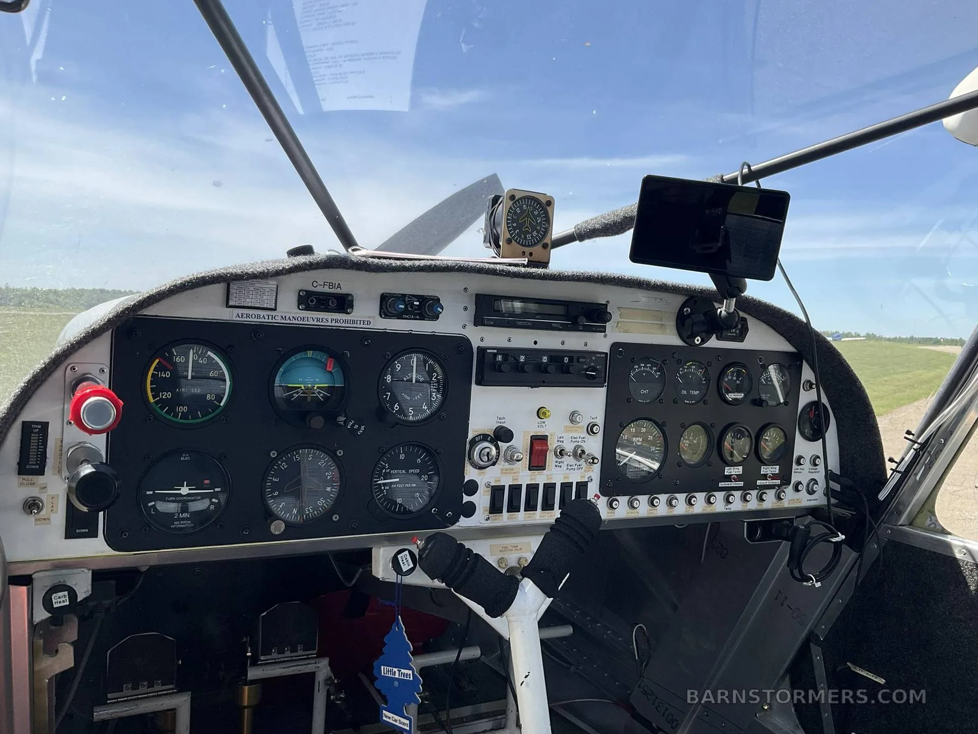 The cockpit instrument panel of a C-FBIA aircraft, showing various gauges and controls, with a view of a grassy field outside.