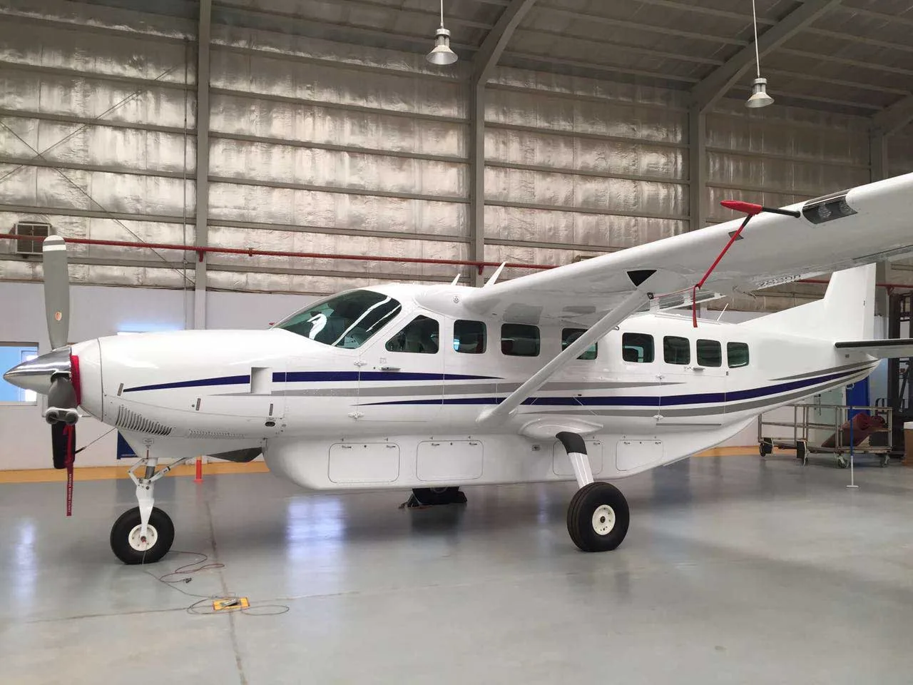A white single-engine turboprop aircraft with blue and grey stripes is parked inside a hangar.