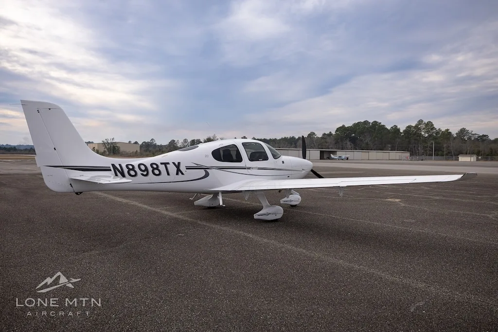 A white Cirrus SR20 aircraft with black and grey stripes, registration N898TX, viewed from the rear left on an asphalt runway.