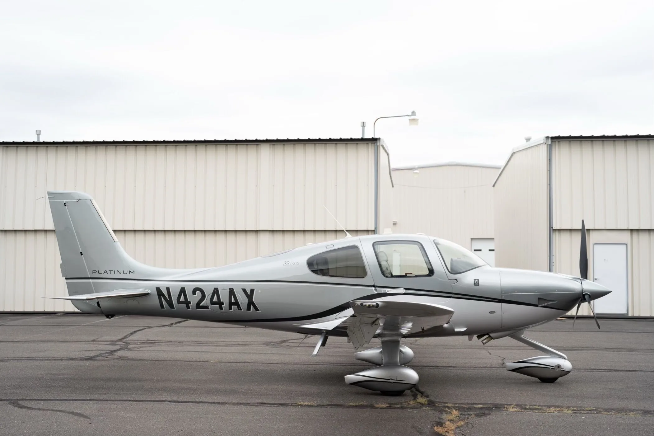 A silver Cirrus SR22 GTS Platinum aircraft, N424AX, is parked on an asphalt tarmac with hangars in the background.