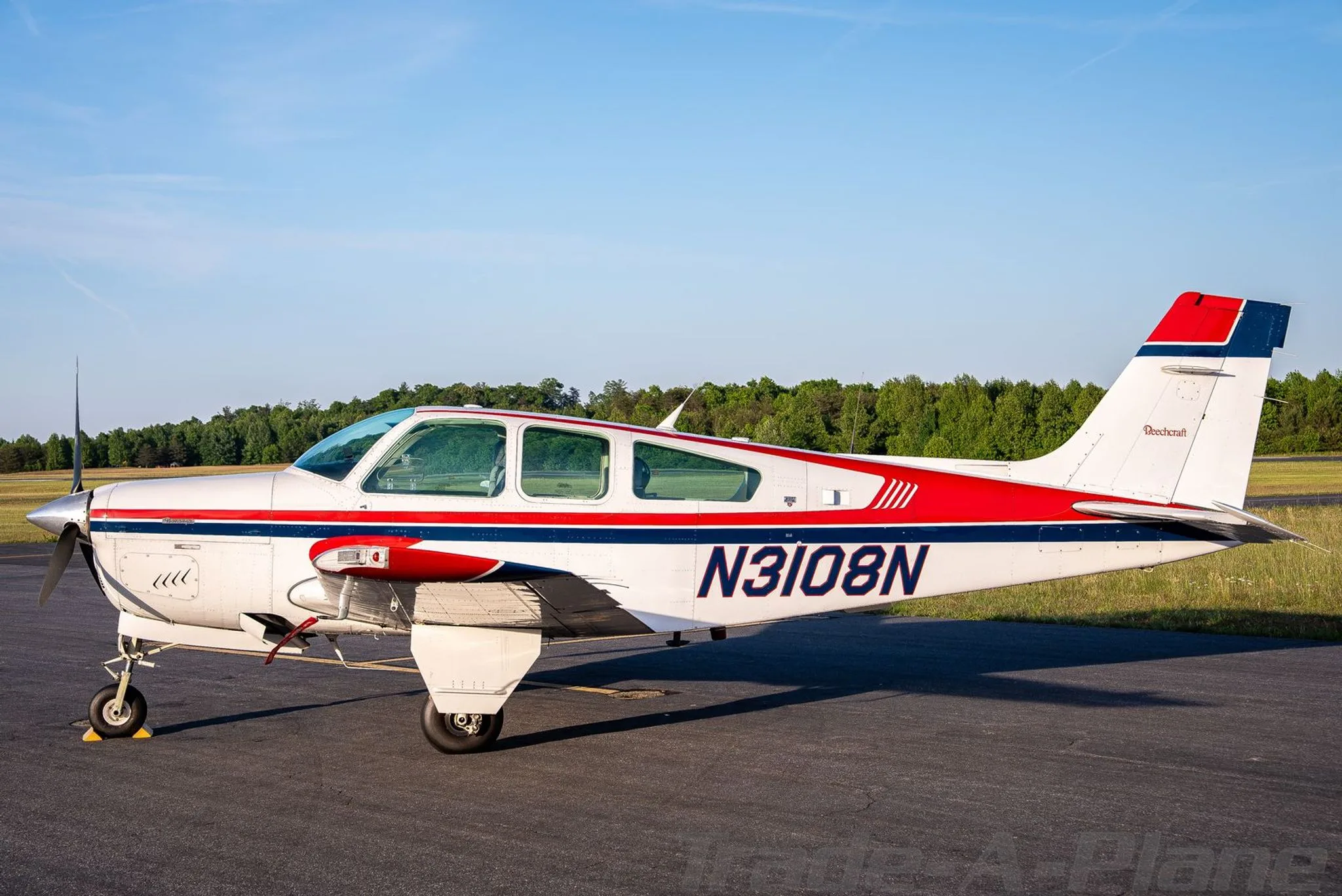 A side view of the white, red, and blue Beechcraft Bonanza N3108N with its registration clearly visible on the fuselage.