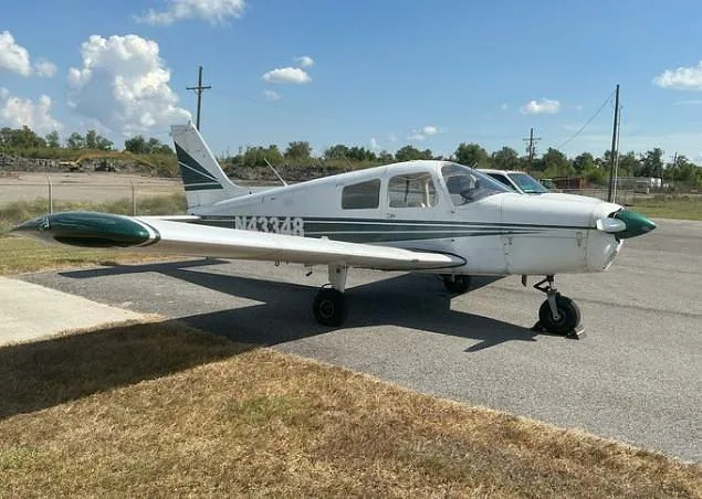 A three-quarter front view of a white Piper Cherokee with green stripes, registration N43348, parked on an asphalt ramp.