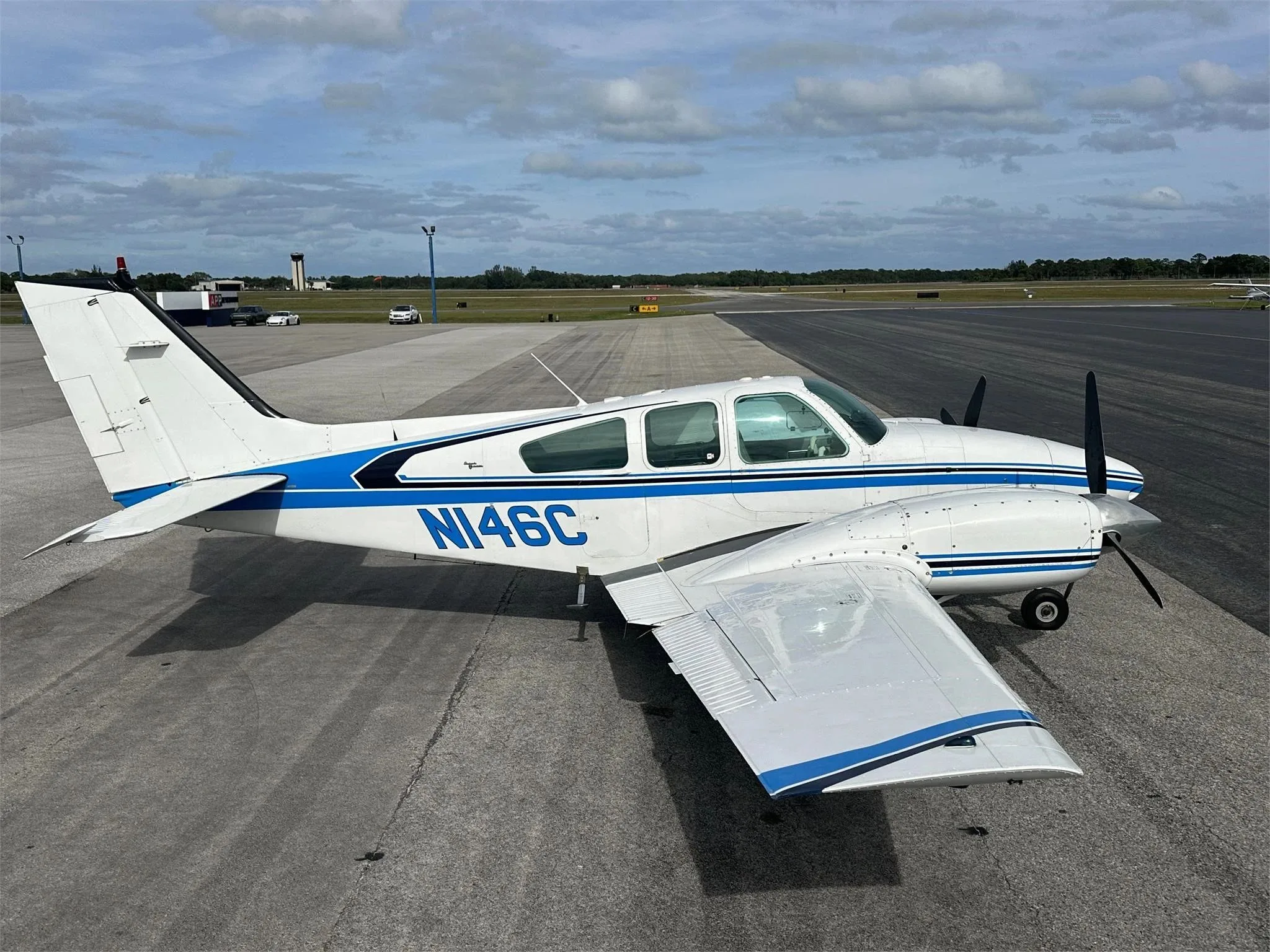 A white and blue twin-engine aircraft, N146C, parked on an airport tarmac under a partly cloudy sky.
