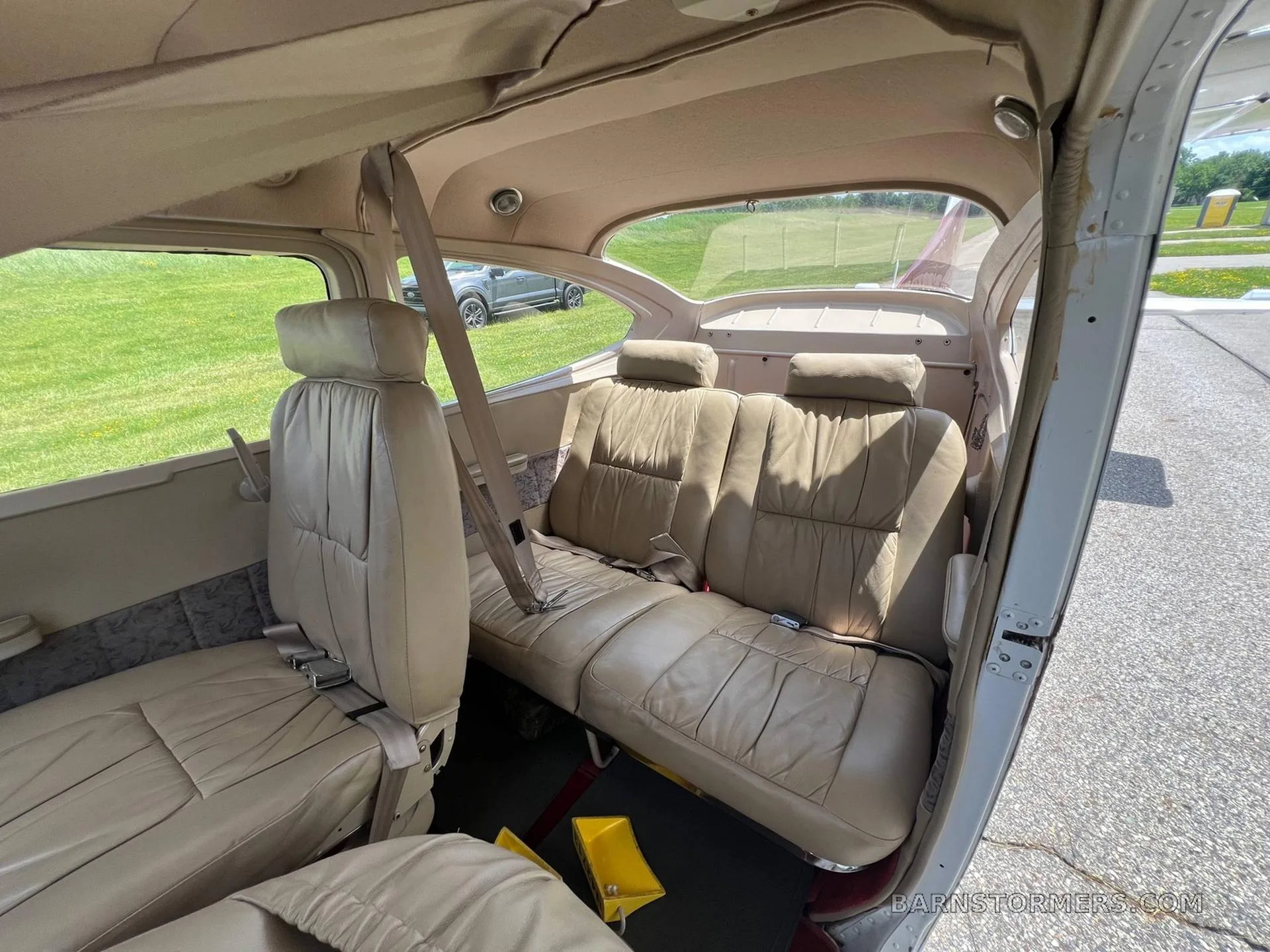 The tan leather interior of a small aircraft cabin showing the rear bench seat and a view of the exterior.