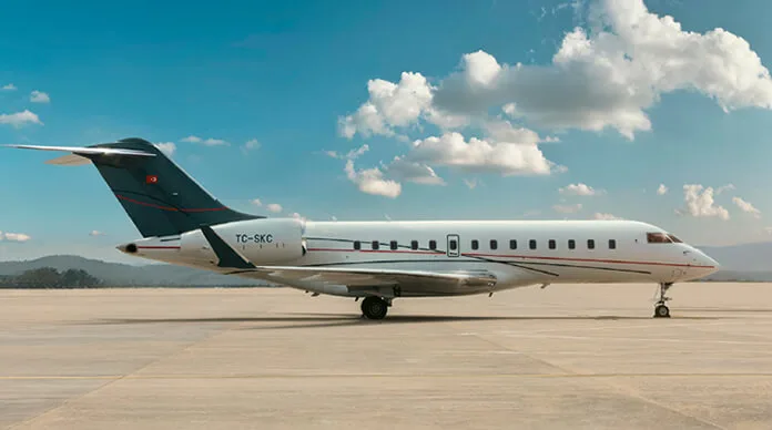 A white business jet with a dark blue tail and red stripe, registration TC-SKC, parked on an airfield under a partly cloudy sky.