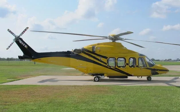 A yellow helicopter with black stripes parked on a concrete pad at an airfield.