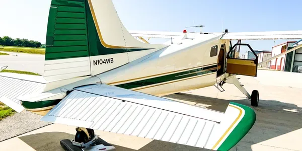 Rear view of the N104WB aircraft, showing its green and white tail and open cabin door on an airfield.
