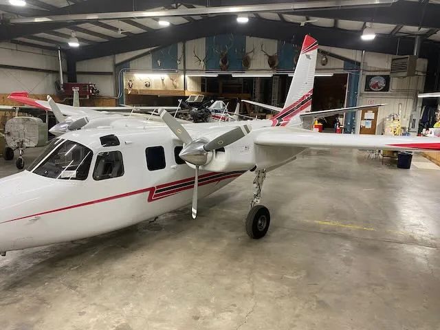 A white twin-engine propeller aircraft with red and black accents is parked inside a hangar.