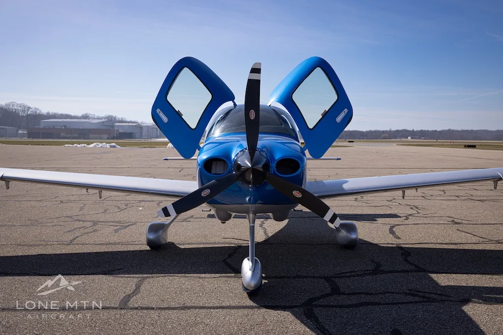 A head-on view of the blue and silver Cirrus SR20 aircraft, registration N270RX, with its doors open on an airport tarmac.