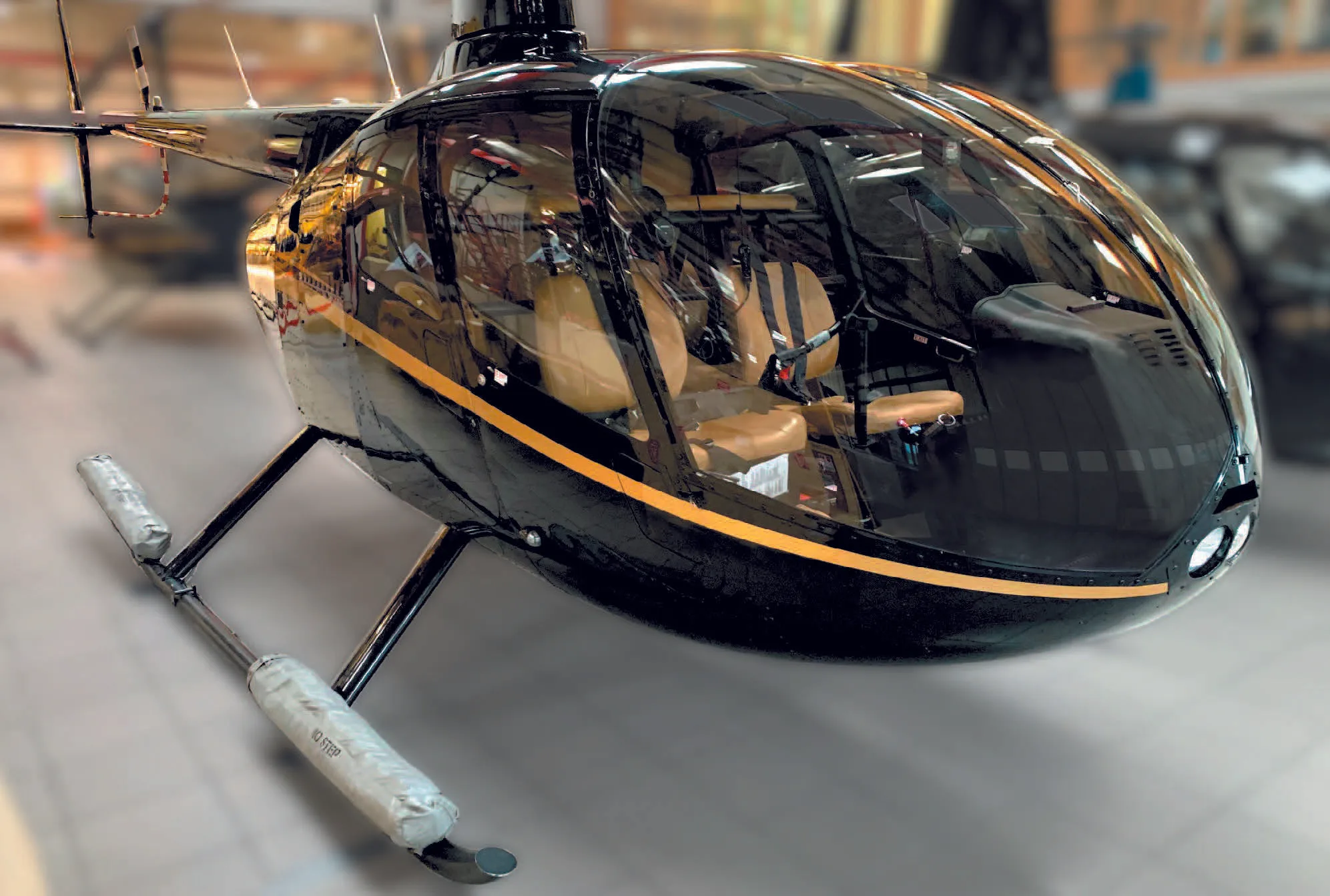 A black Robinson R66 Turbine helicopter with a gold stripe sits in a hangar, viewed from the front-right.