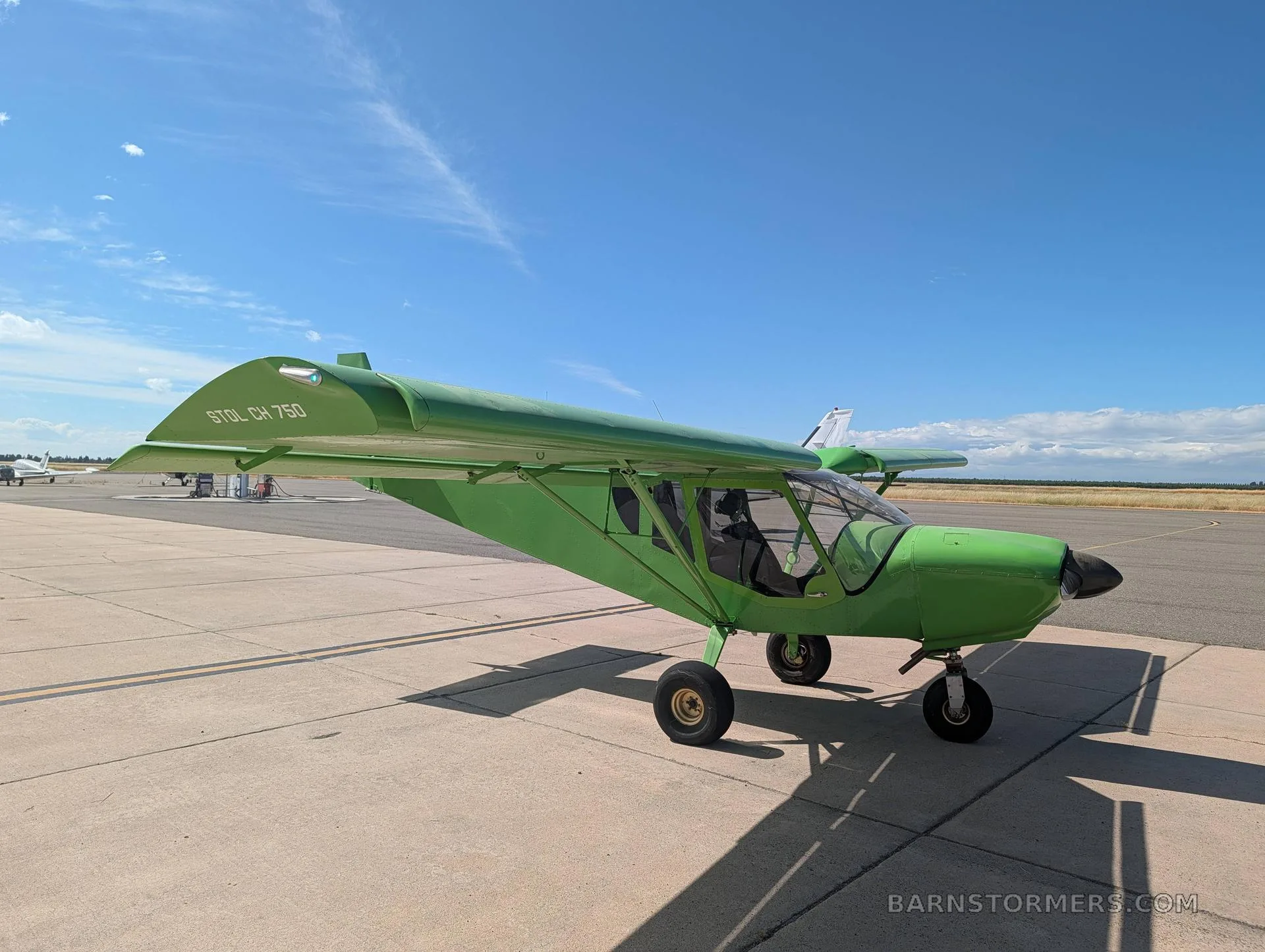A bright green Zenith STOL CH 750 aircraft parked on an airfield tarmac under a blue sky.