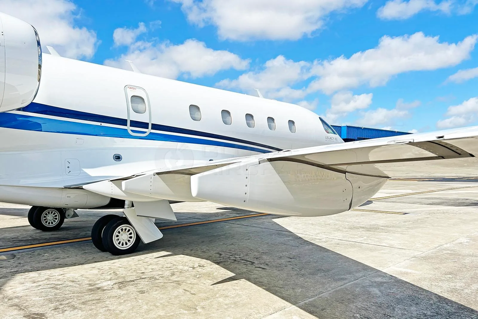 Side view of the fuselage and wing of a white Embraer Legacy 450 business jet with blue stripes.