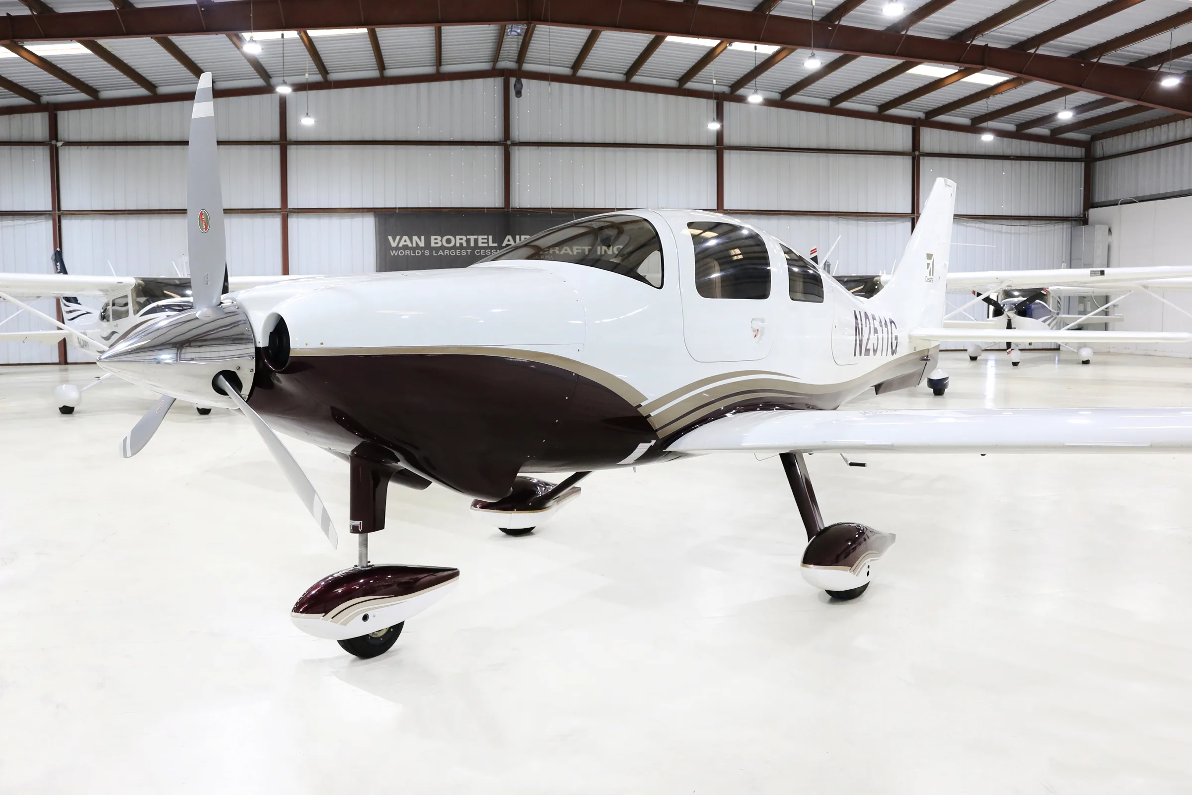A white and brown single-engine propeller aircraft, N2511G, is parked in a hangar, viewed from the front-left.