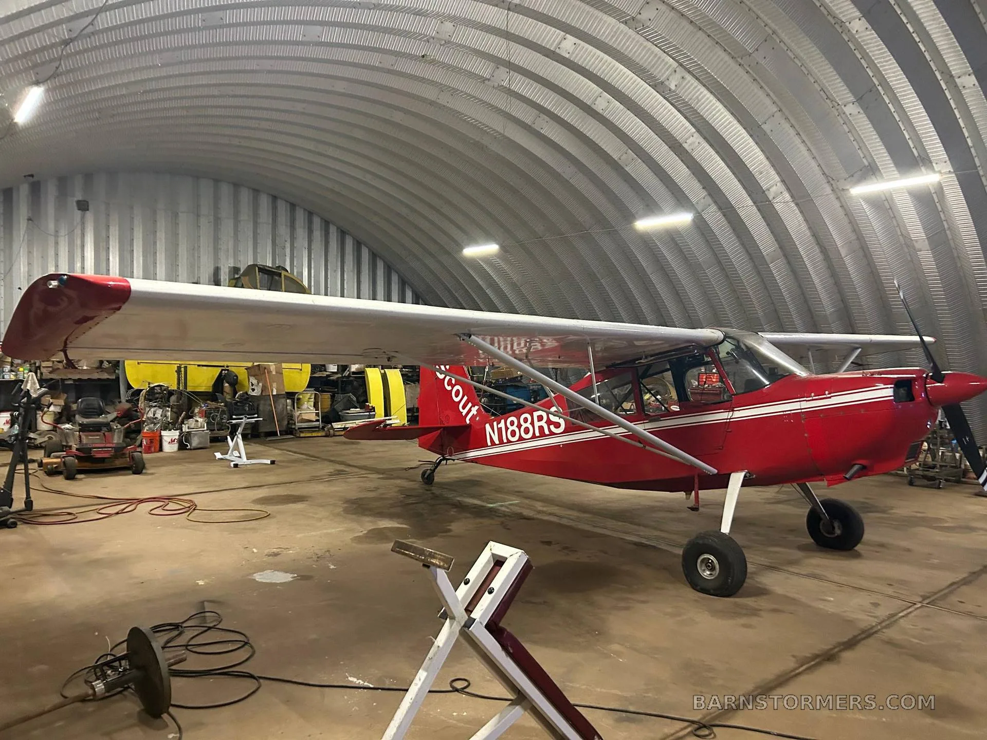 A red Scout N188RS aircraft with white stripes is parked inside a metal hangar, viewed from the left side.