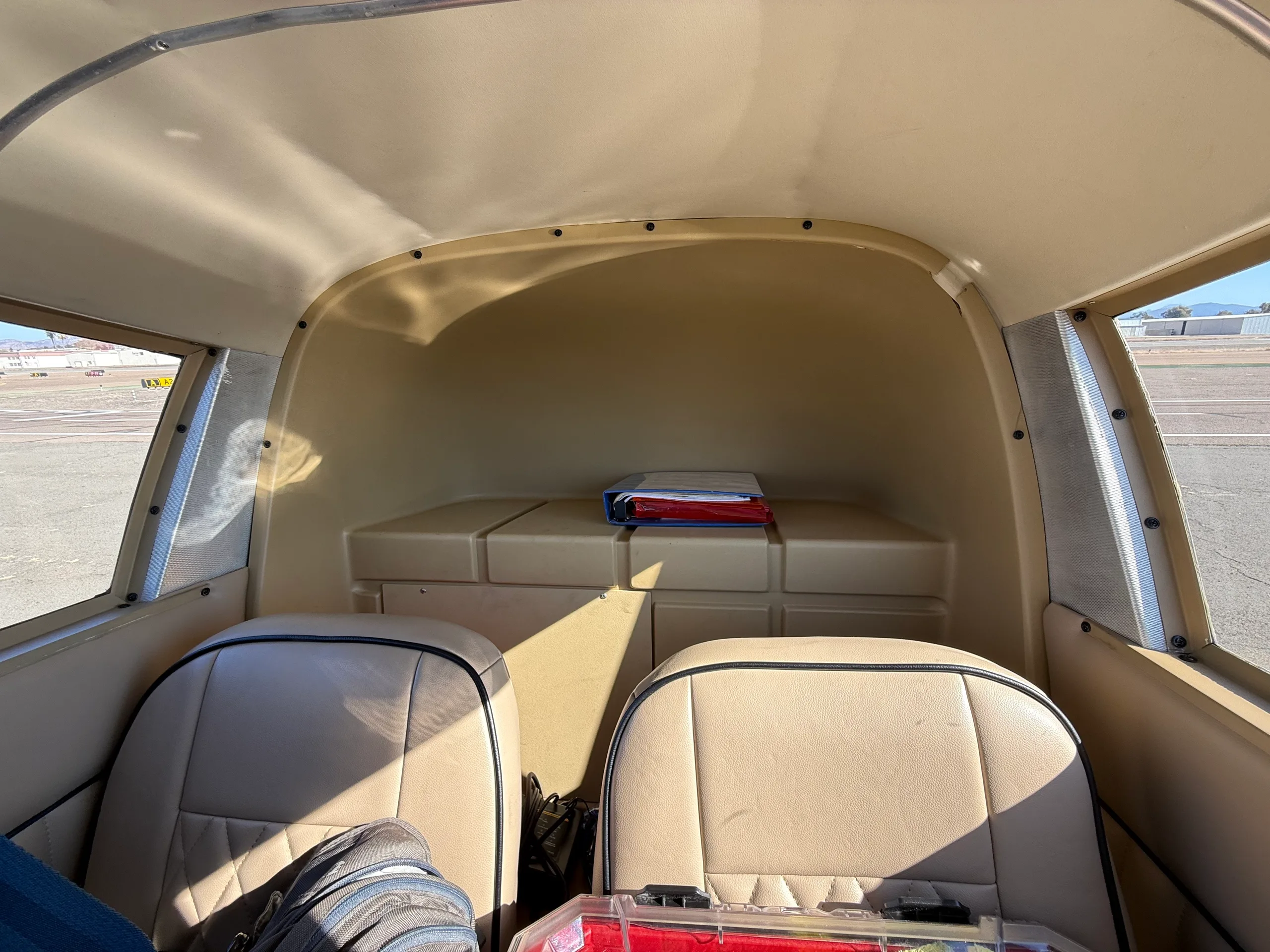 The beige interior cabin of a small aircraft, showing the rear seats and storage area.