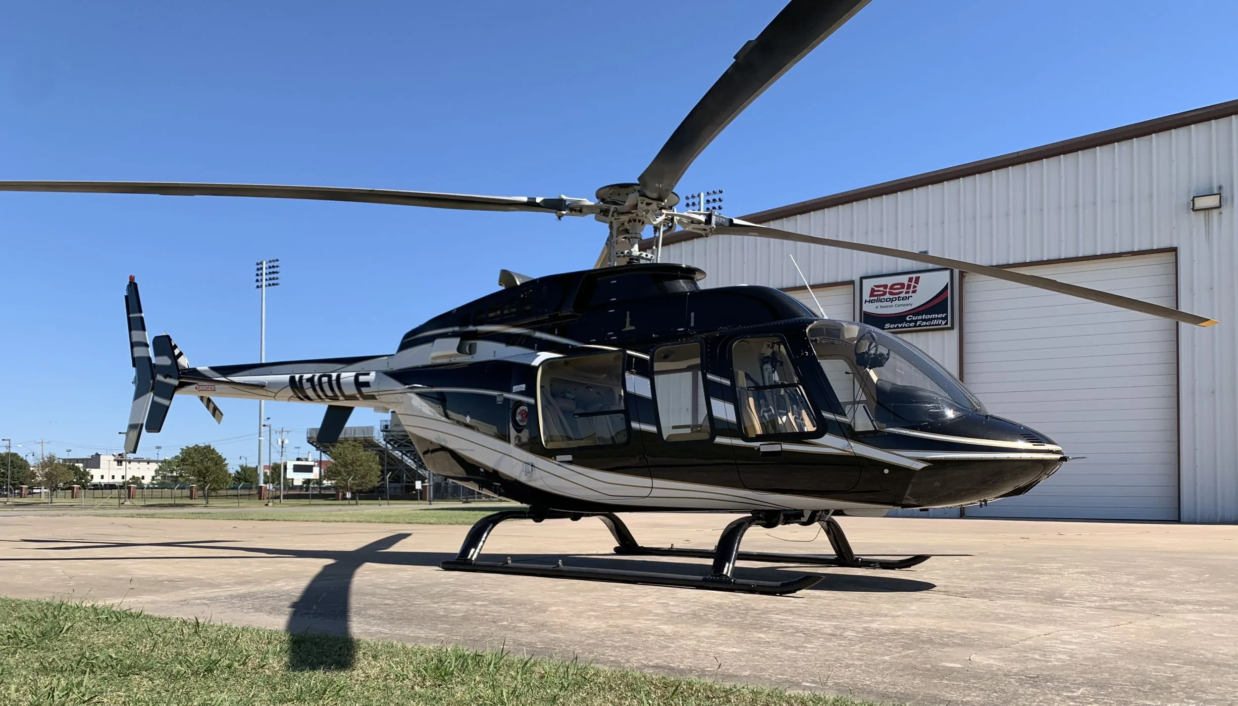 A black and white Bell helicopter, registration N10LF, parked on a concrete pad in front of a hangar on a sunny day.