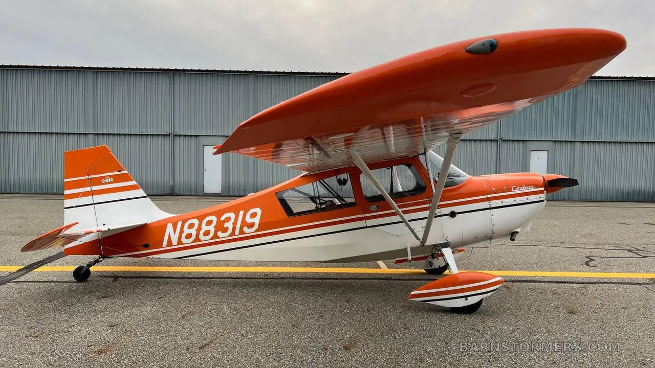 A side view of an orange and white Cessna 170B aircraft with tail number N88319 parked on an asphalt apron.