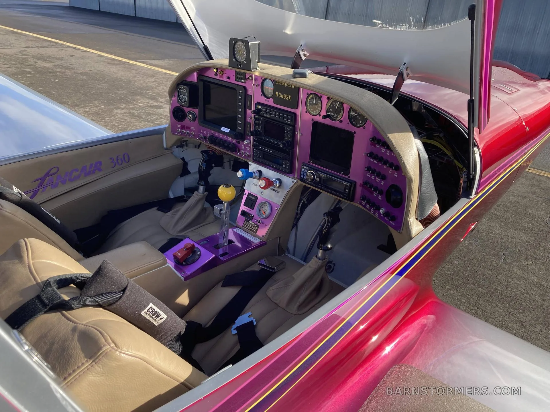 The cockpit of a Lancair 360 aircraft, featuring a purple instrument panel with multiple screens and gauges, and tan leather seats.