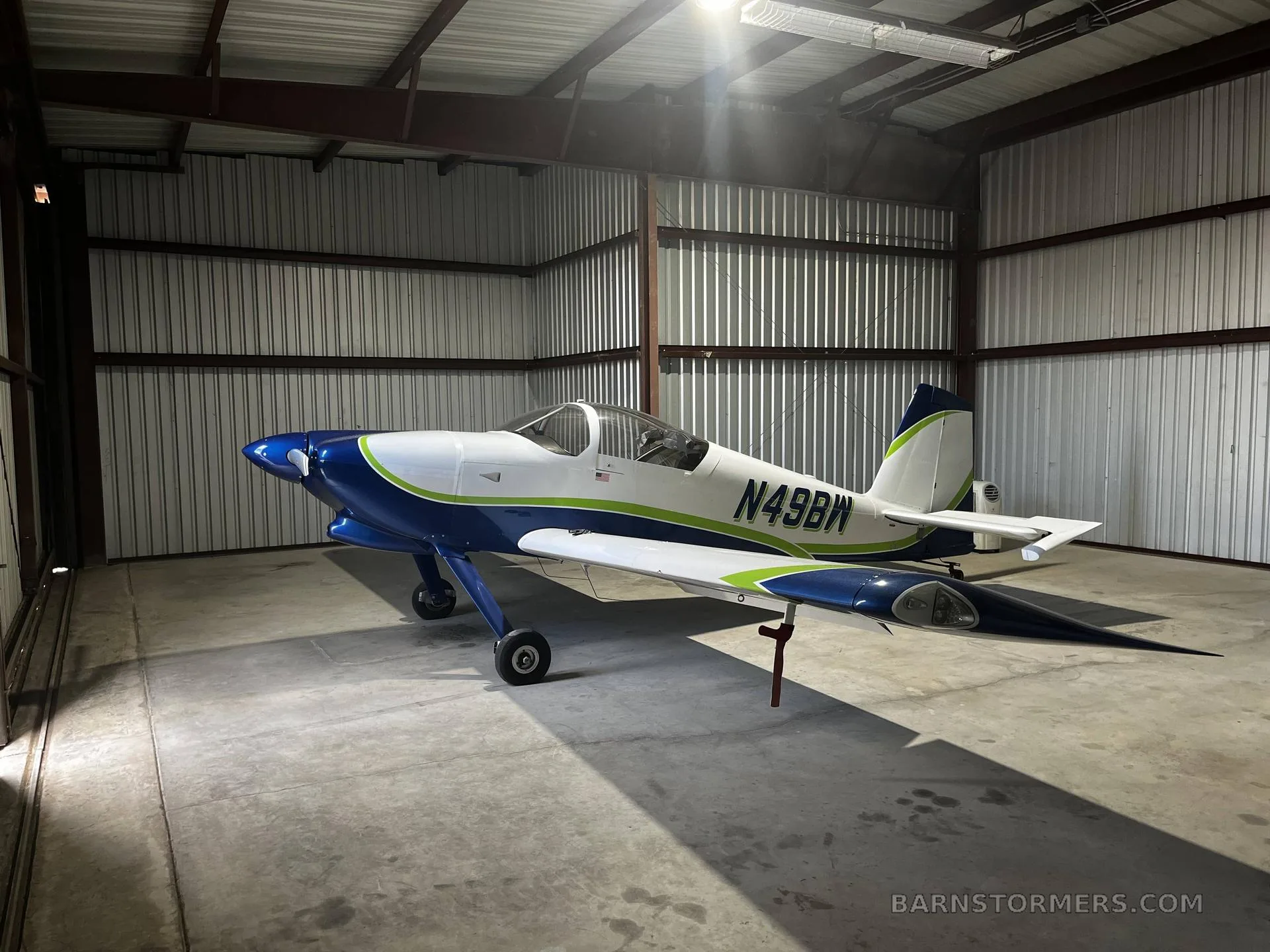The blue and white experimental aircraft N49BW parked inside a metal hangar.