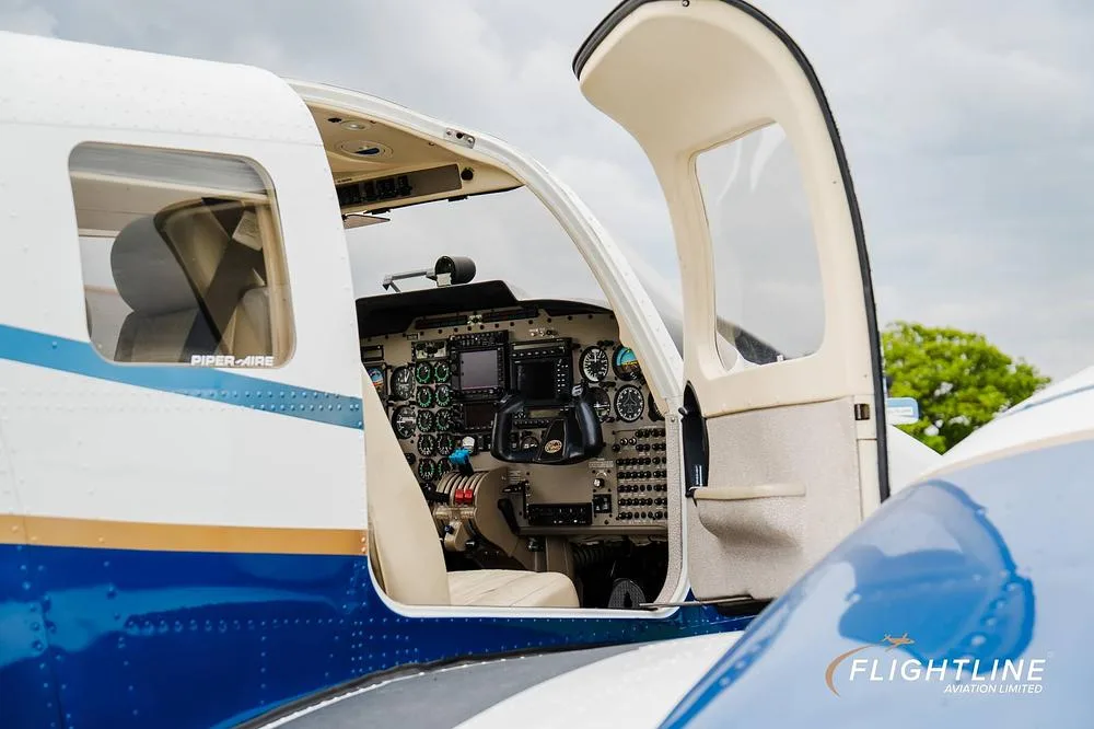 The open door of a Piper Seneca aircraft revealing the cockpit with its instrument panel and pilot's seat.
