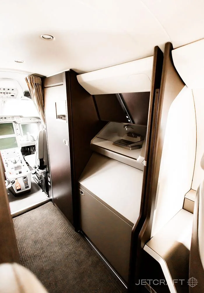 The aircraft's galley area with storage compartments, looking towards the cockpit entrance.