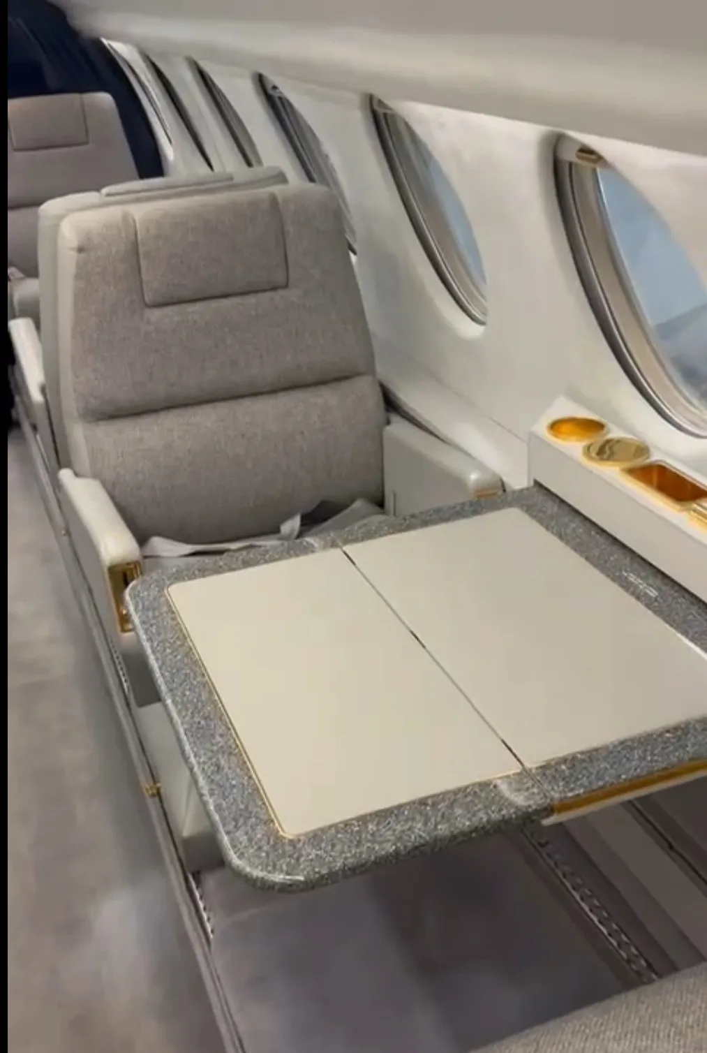 A close-up of an aircraft's grey interior seat and a fold-out table with a speckled surface.