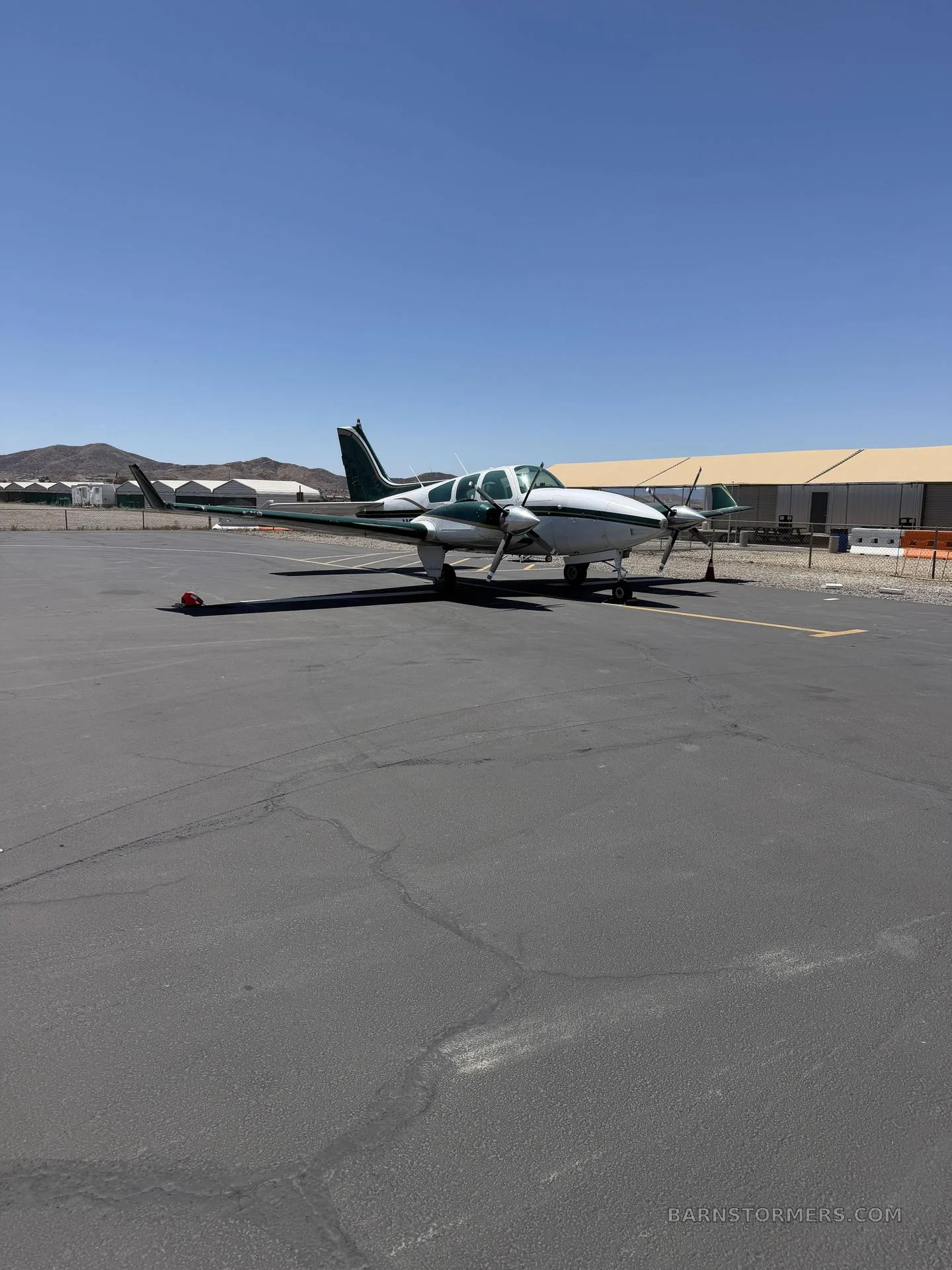 A white and green twin-engine propeller aircraft (N677Z) parked on an asphalt ramp with mountains in the background.